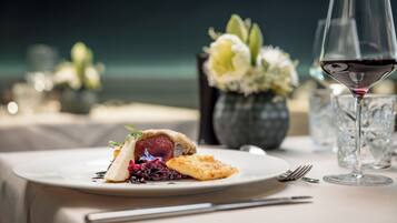 Une table à manger avec une assiette de nourriture, un verre de vin rouge et un vase rempli de fleurs.