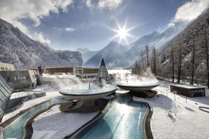 A modern spa with a hot tub, a pool, and a mountain backdrop.