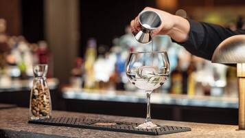 Un barman sirviendo una bebida en un vaso con una ramita de romero.