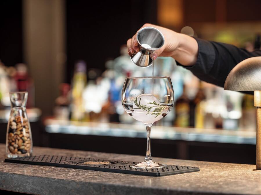 Un barman sirviendo una bebida en un vaso con una ramita de romero.