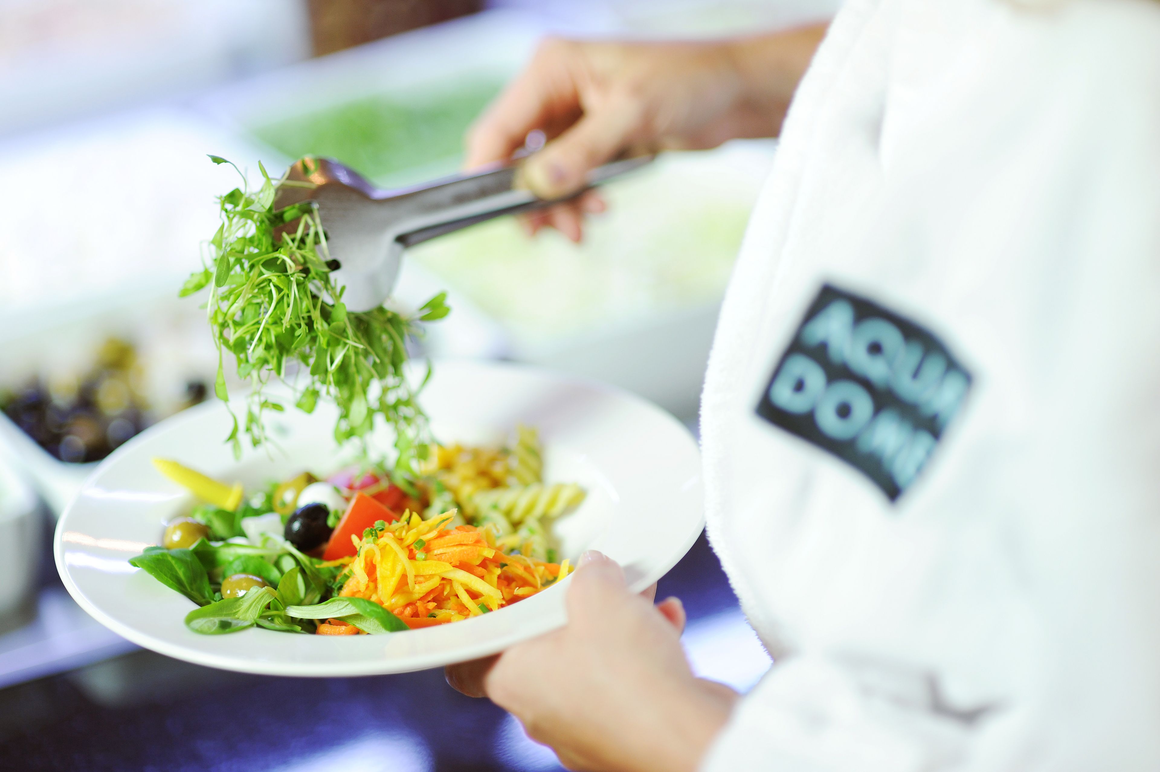 A person in a white uniform with a name tag, holding a plate with a salad.