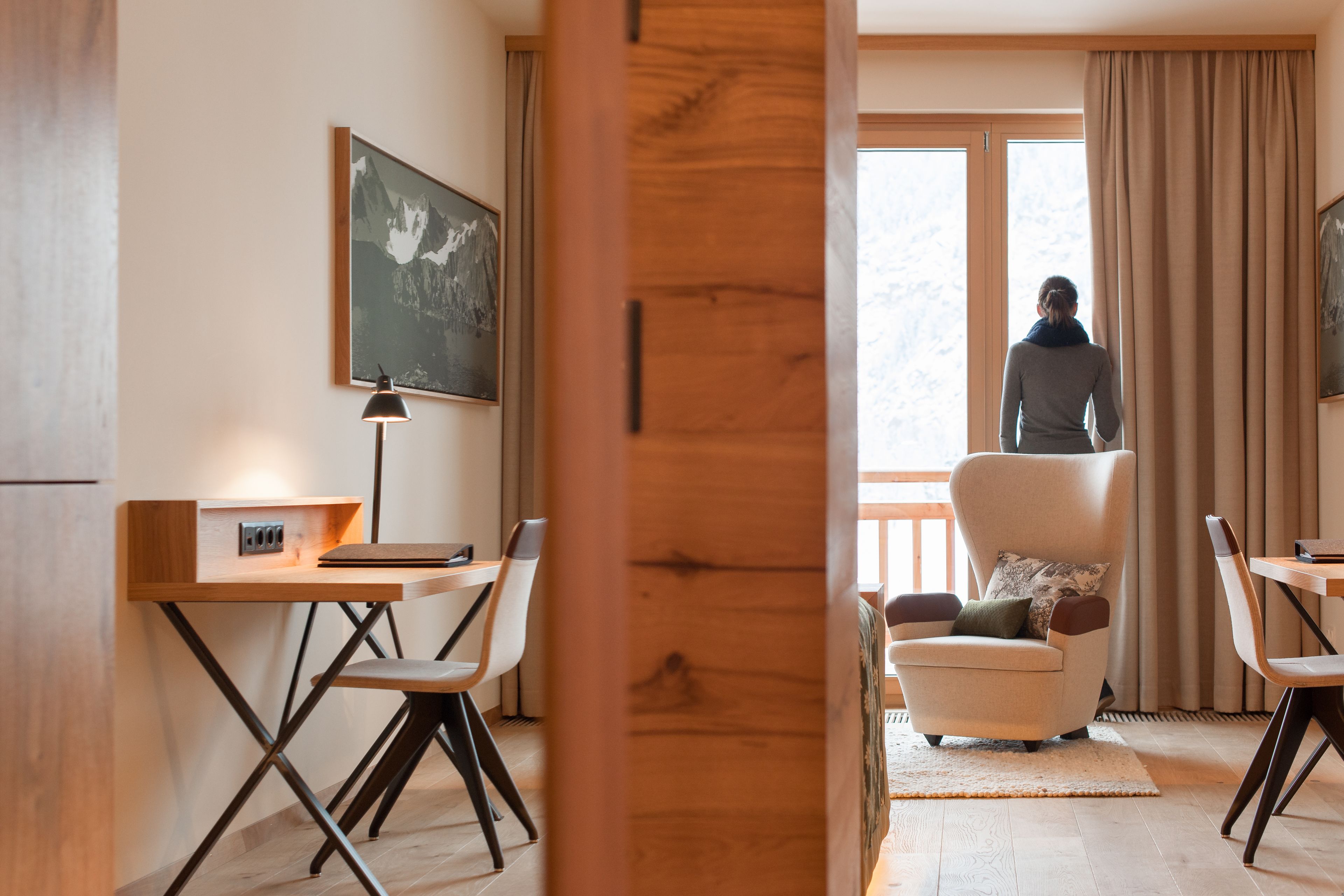 A modern room with a wooden desk, a chair, a sofa, and a large window with curtains.