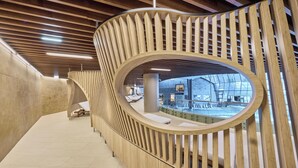 Un intérieur moderne avec un garde-corps en bois aux lignes courbes, un espace vitré offrant une vue dégagée et un sol carrelé.