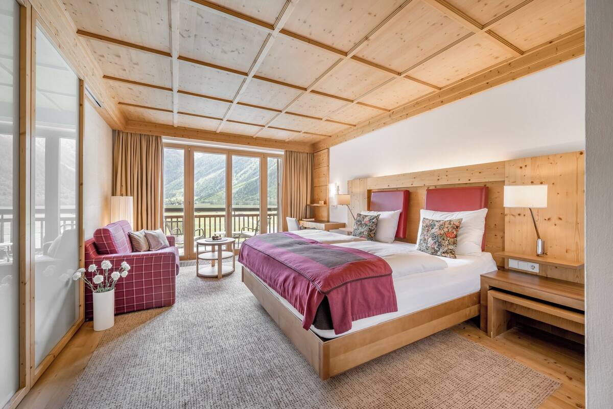 A hotel room with a large bed, a seating area with a sofa and chairs, a small table, and a view of the outdoors.
