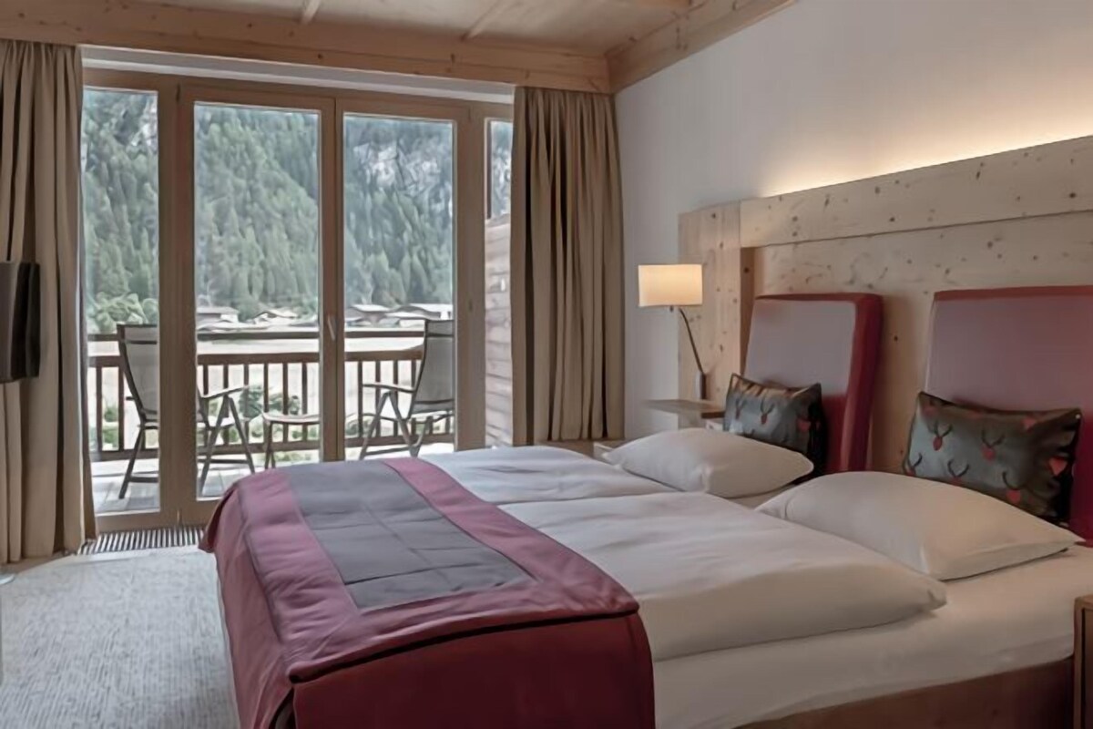 Een hotelkamer met twee bedden, een groot raam en een balkon met stoelen.