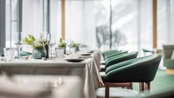 A restaurant with tables set for dining, featuring green upholstered chairs and a vase with flowers.
