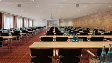 A conference room with rows of tables, chairs, and water bottles, featuring a red carpet and a wooden wall.
