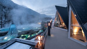 Un hôtel moderne doté d’une piscine à débordement entièrement vitrée, d’un espace dédié aux sources chaudes et offrant une vue sur des montagnes enneigées.