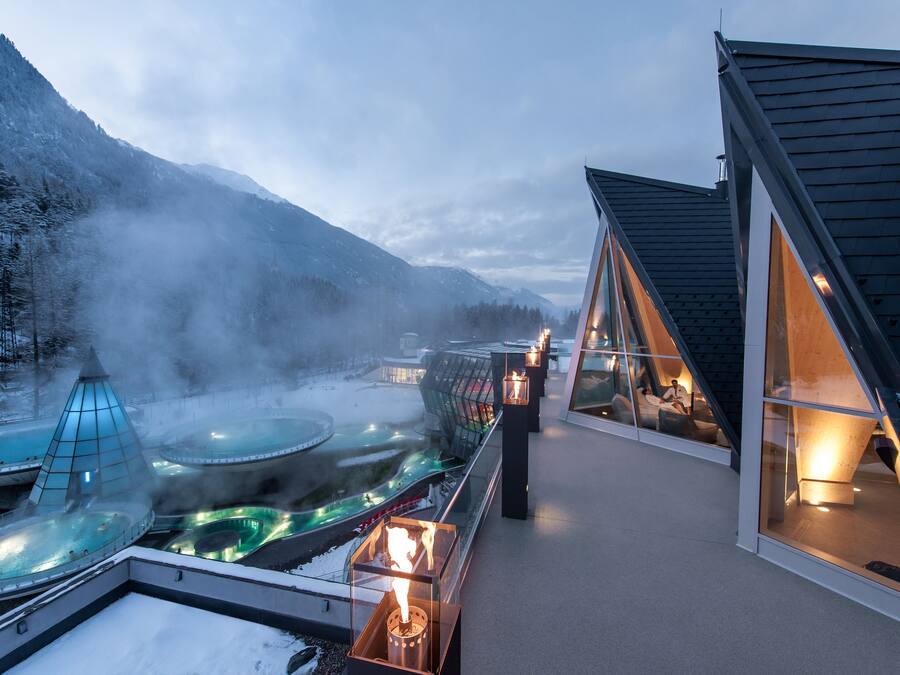 Um hotel moderno com piscina infinita em vidro, área de águas termais e vista para montanhas cobertas de neve.