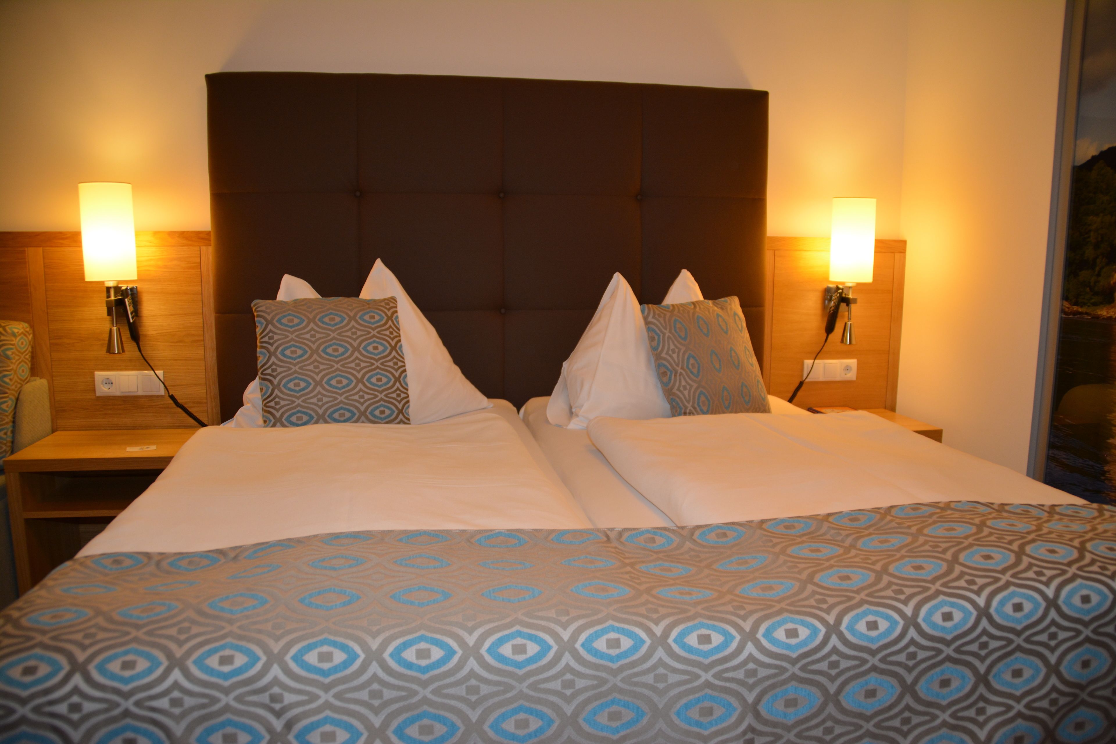 A double bed with a patterned bedspread, two bedside tables with lamps, and a wooden headboard.