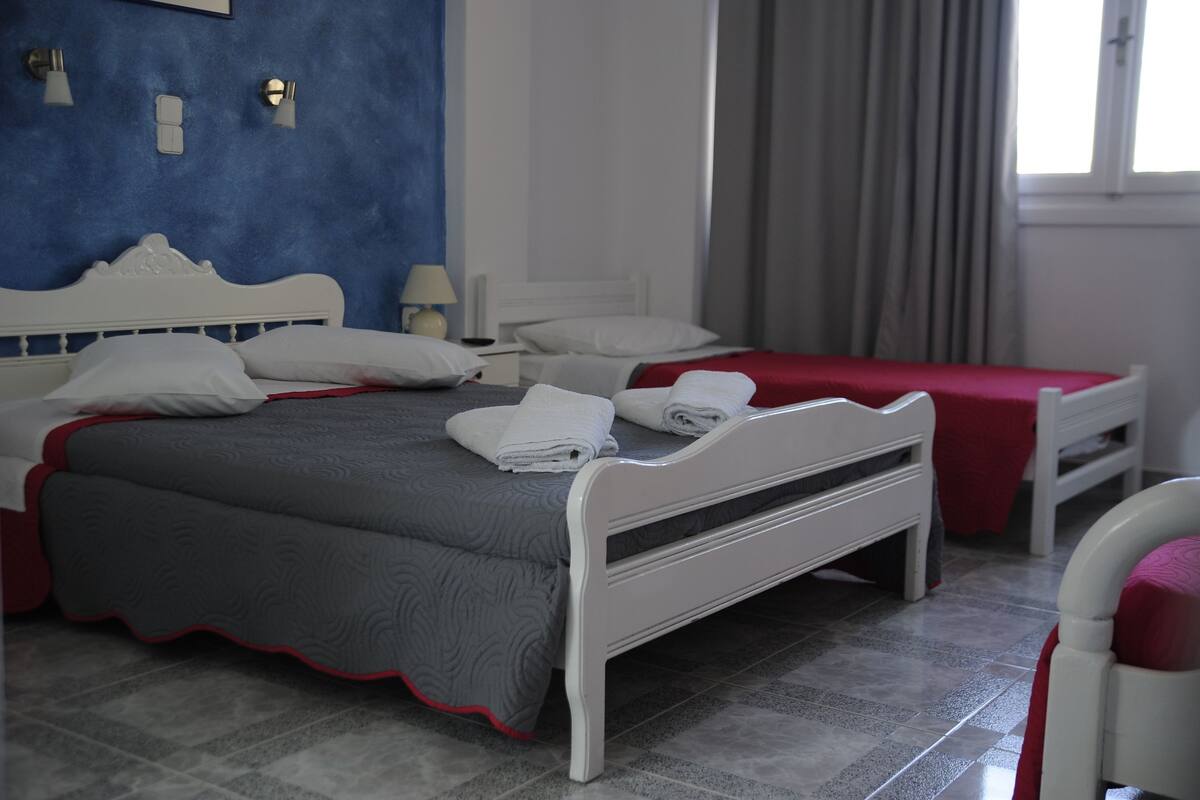 A double bed with a grey and red bedspread, white headboard, and two bedside tables with lamps.
