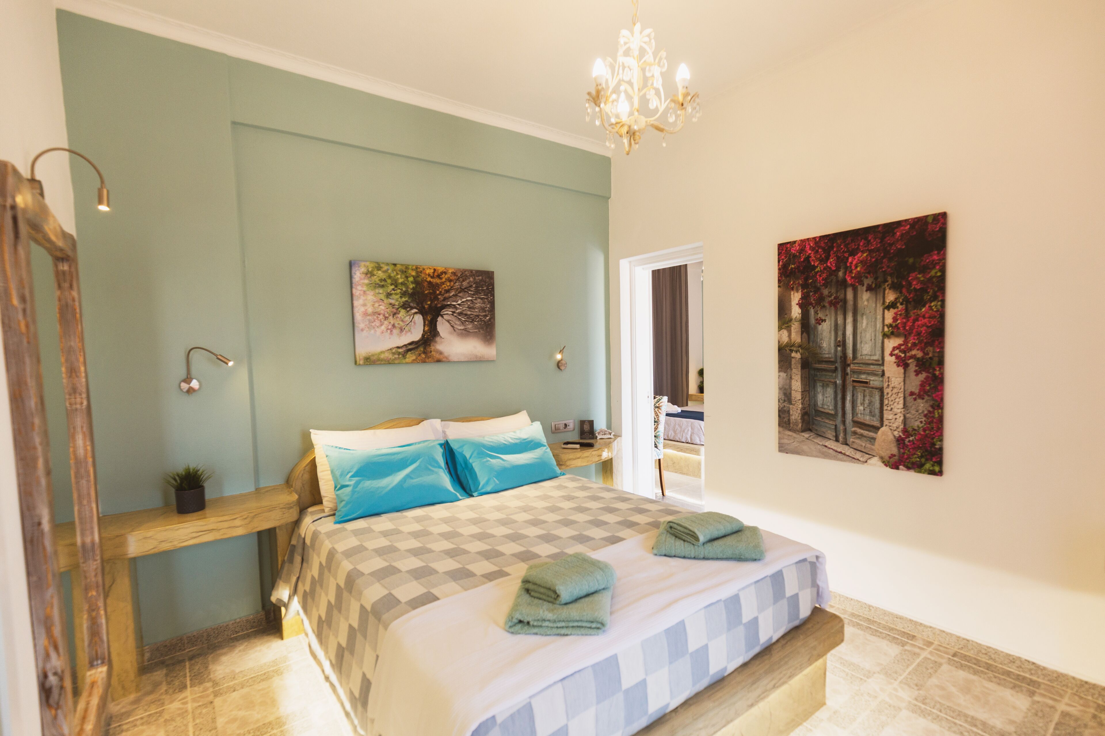 Ein Schlafzimmer mit karierter Bettdecke, einer hölzernen Bank, einem Kronleuchter und zwei Bildern an den Wänden.