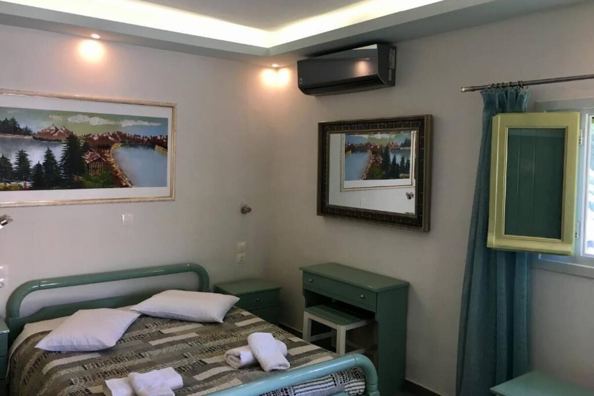 A bedroom with a bed, bedside table, a small desk, and a wall-mounted air conditioner.