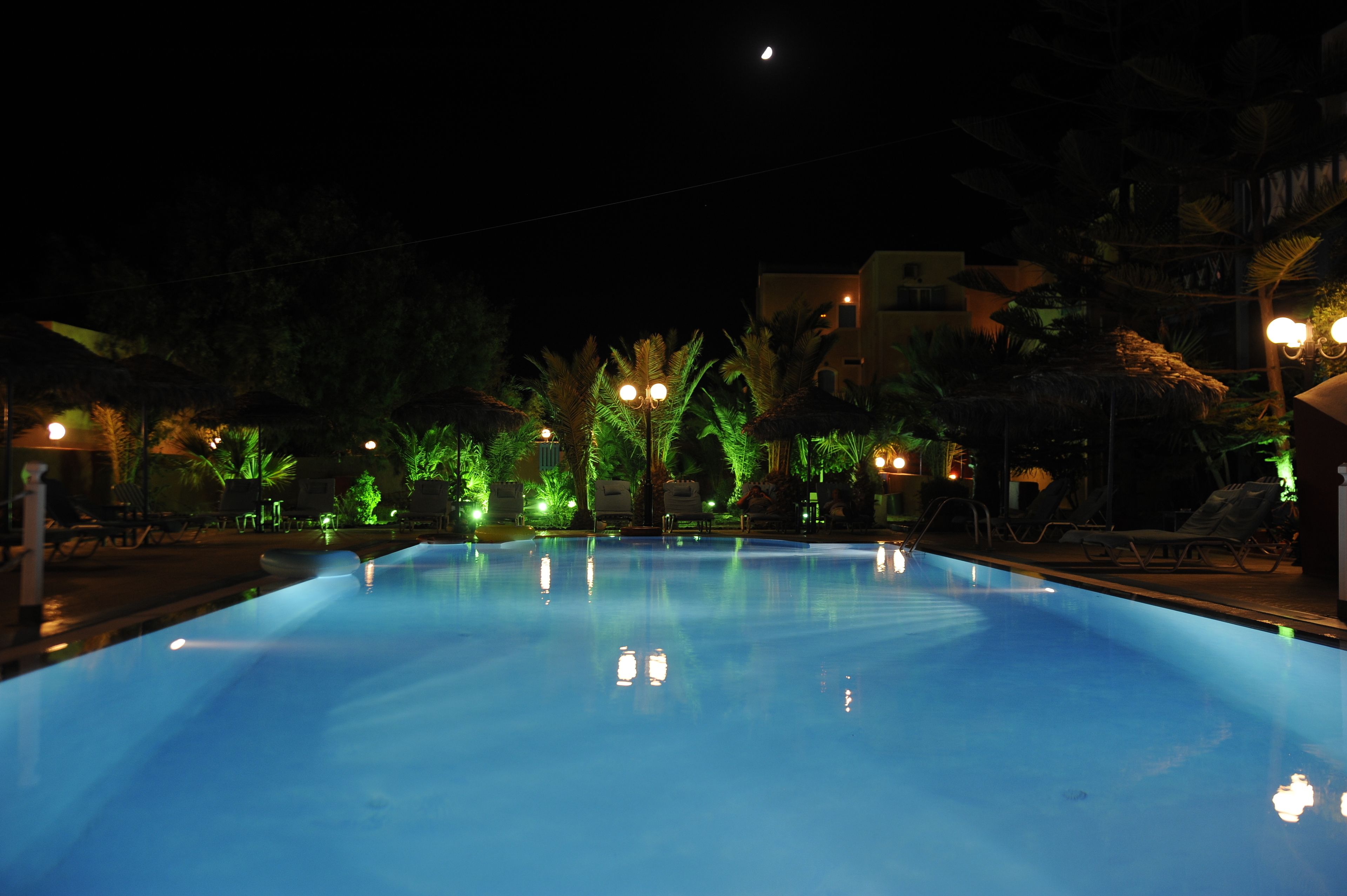 A nighttime pool area with a clear pool, lounge chairs, and palm trees.