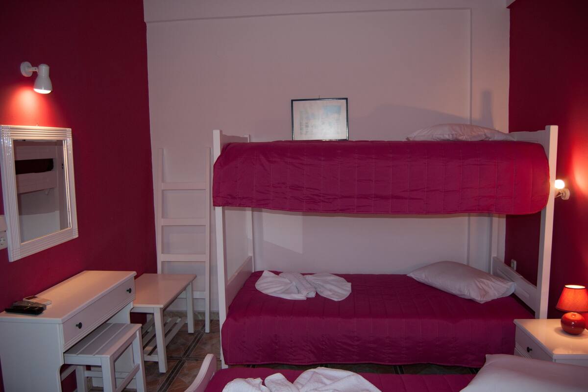 A room with a bunk bed, a desk, a chair, a mirror, and a bedside table with a lamp.