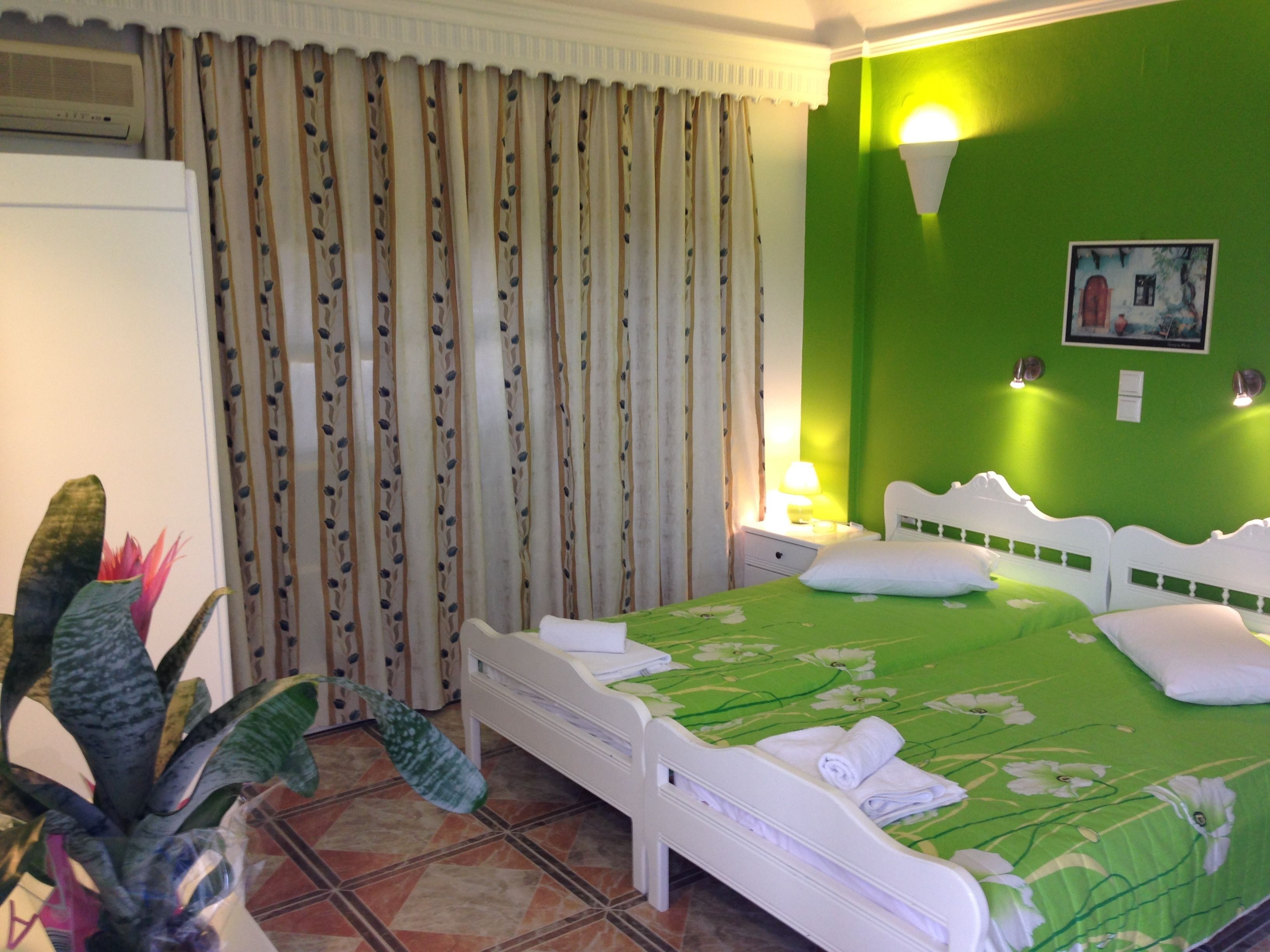 A room with a bed, curtains, a nightstand, a lamp, a wall-mounted light, a potted plant, and a painting on the wall.
