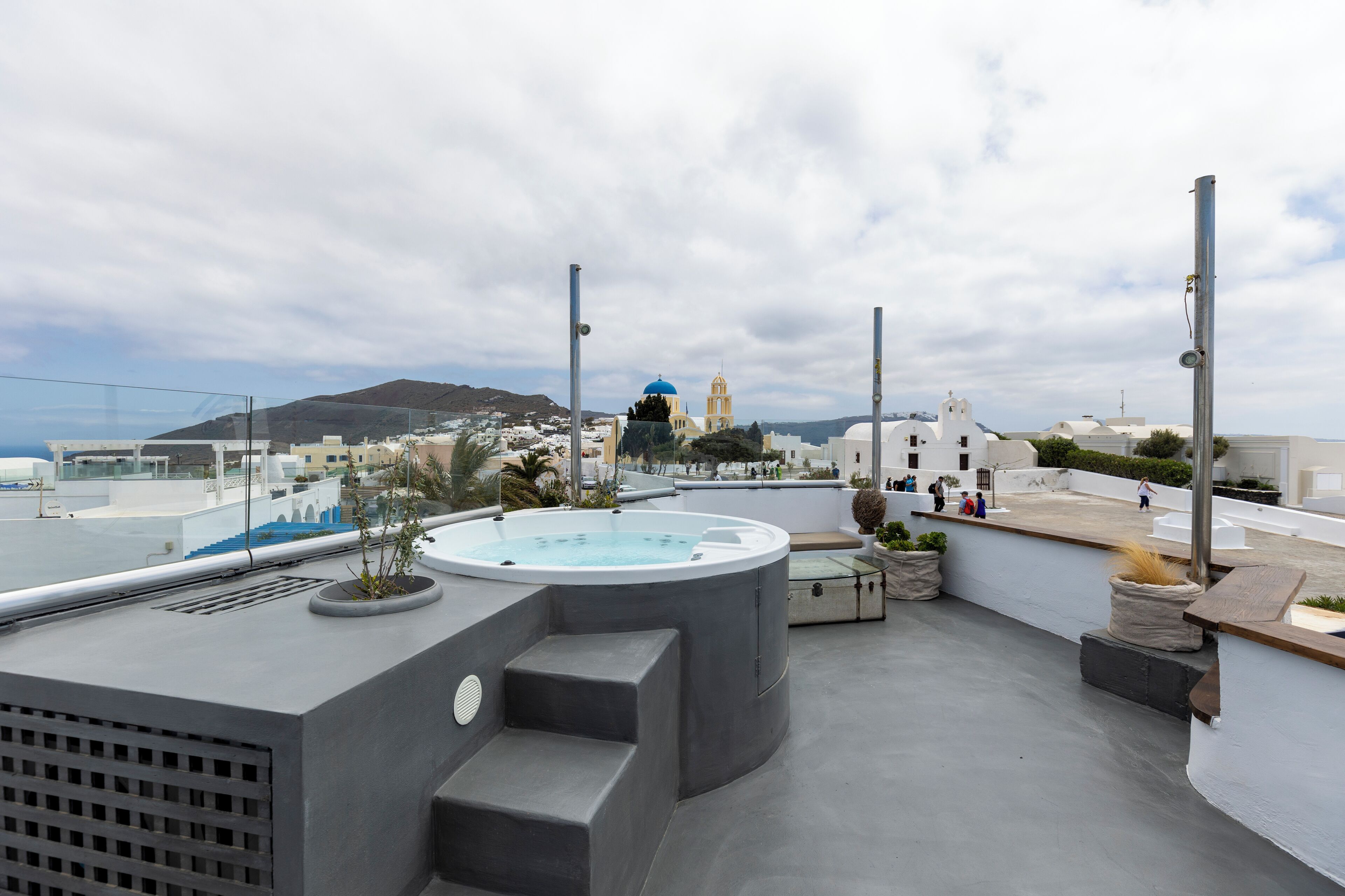 A rooftop terrace with a hot tub, steps, and a view of a coastal town with white buildings and a blue-domed church.
