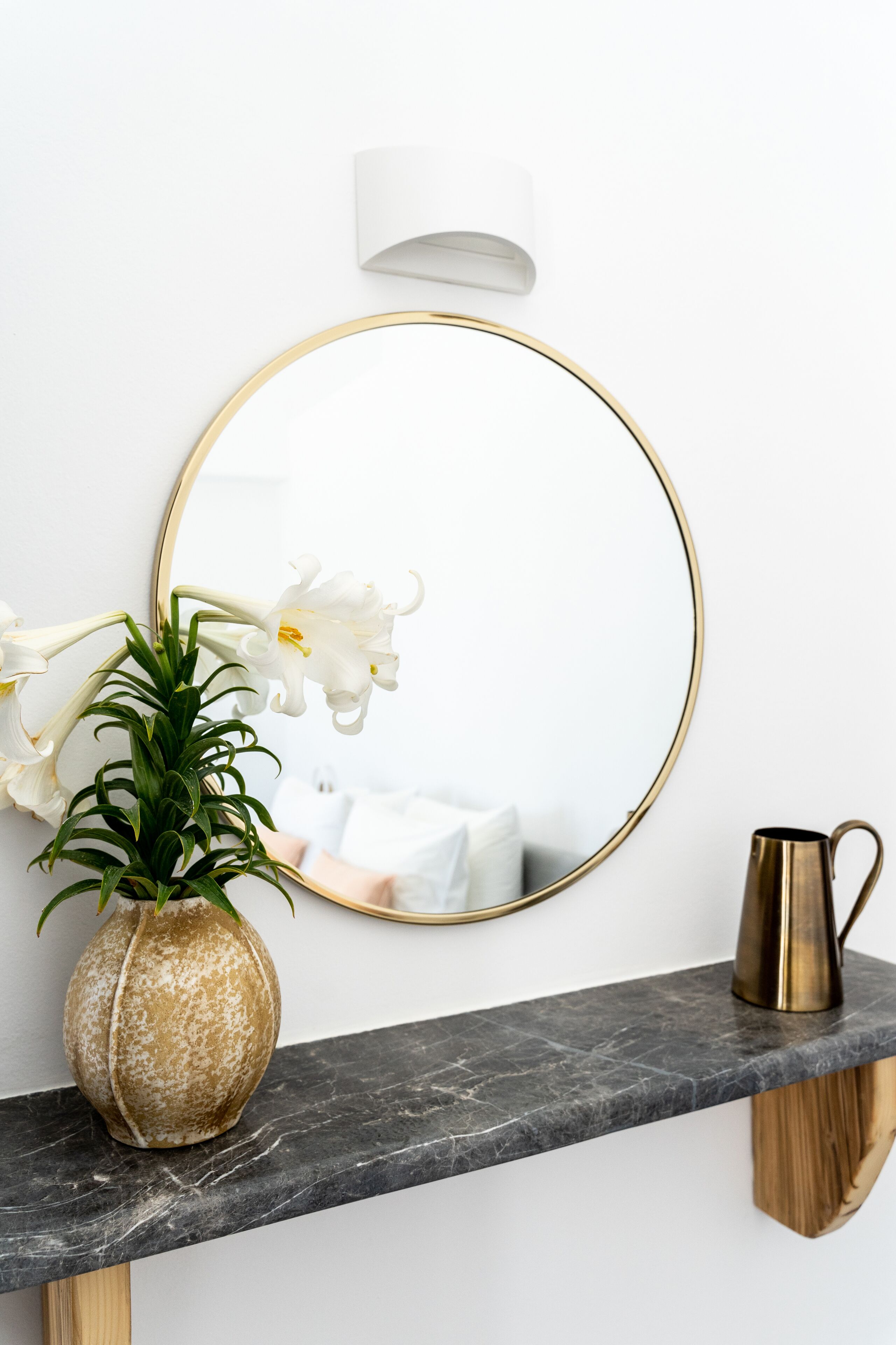 A bathroom vanity with a marble countertop, a gold-framed mirror, a white orchid vase, and a gold pitcher.