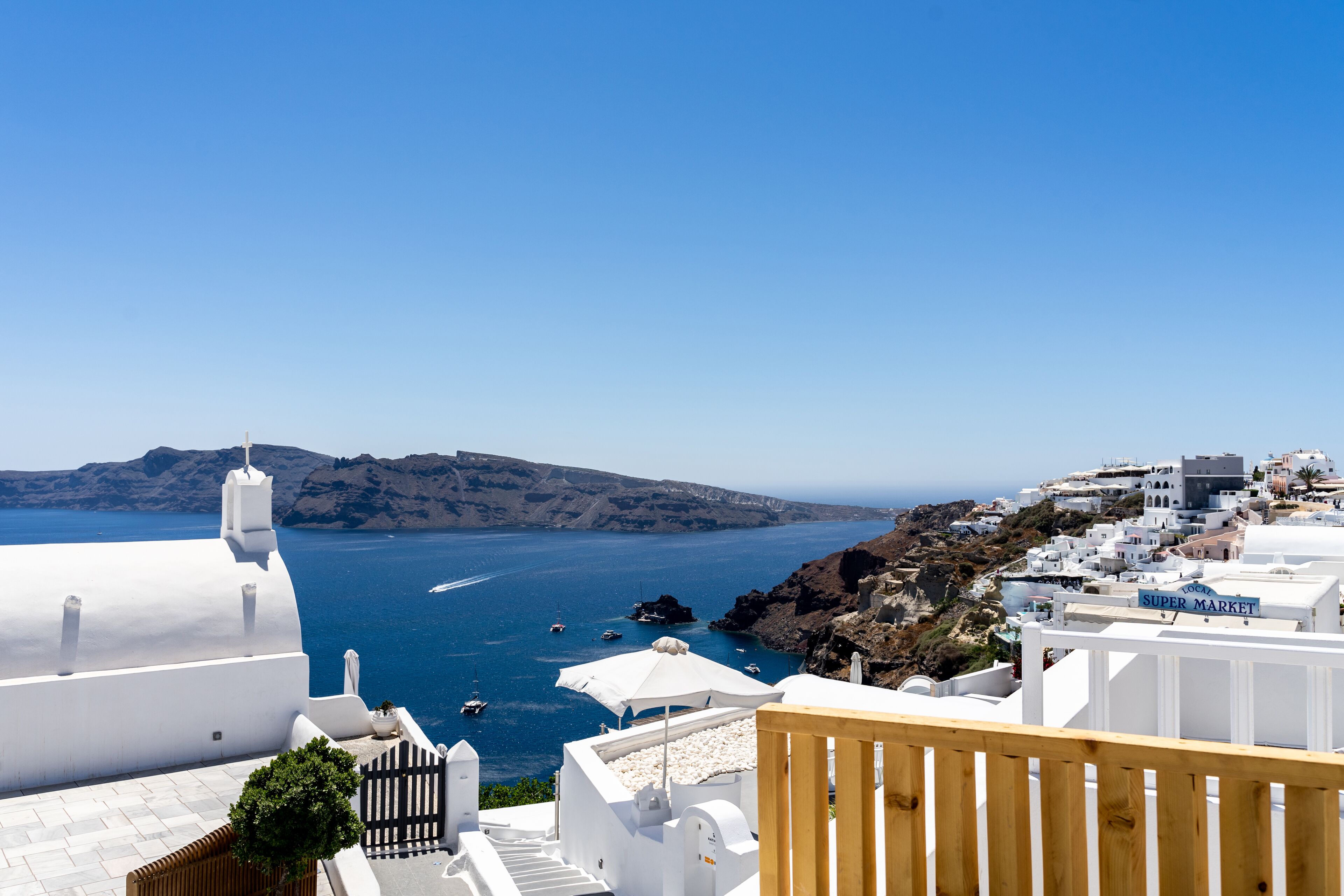 A coastal town with white buildings, a wooden deck, and a view of the sea with boats.
