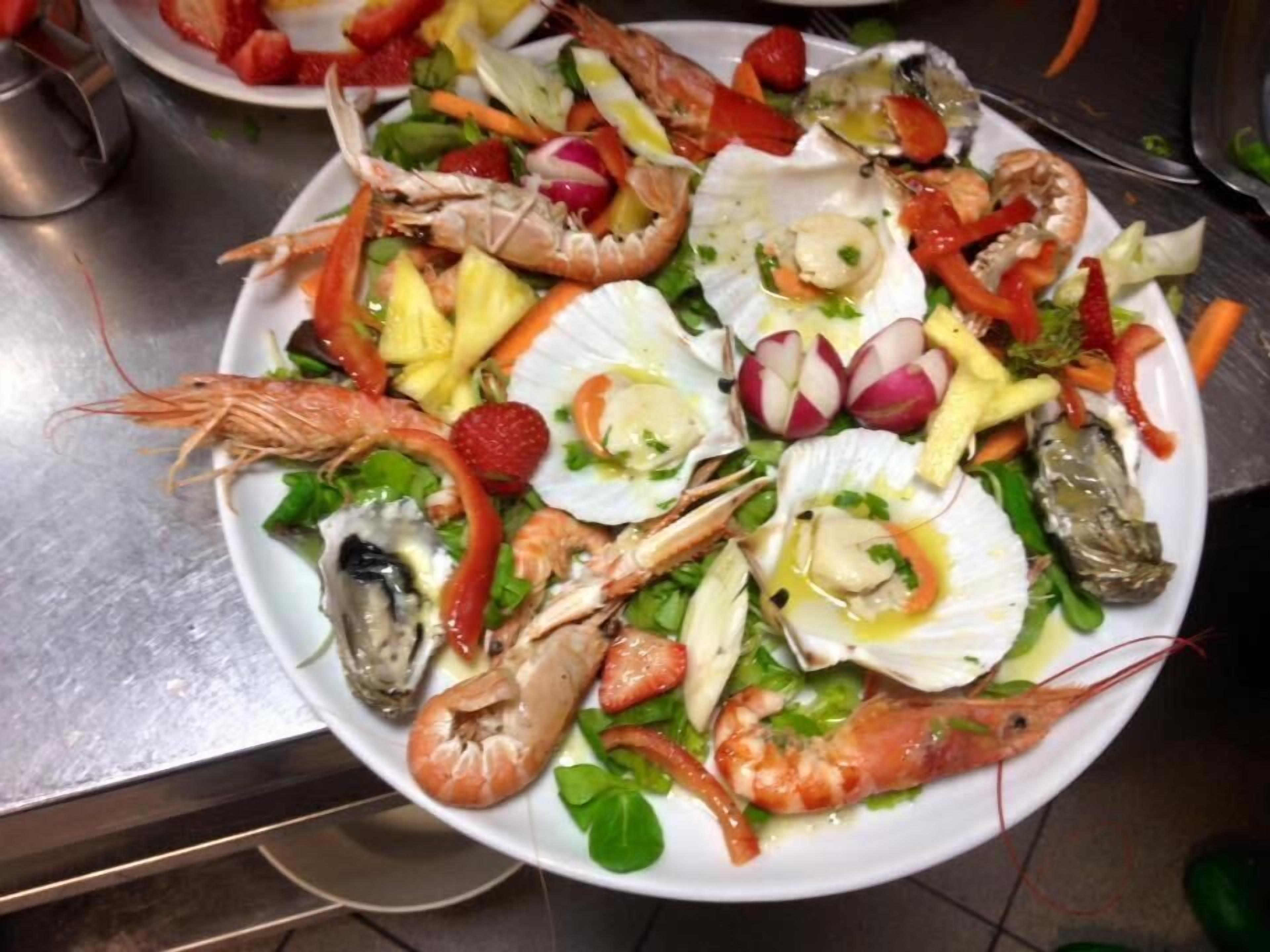 Uma travessa de frutos do mar com camarões, ostras e legumes em um prato.