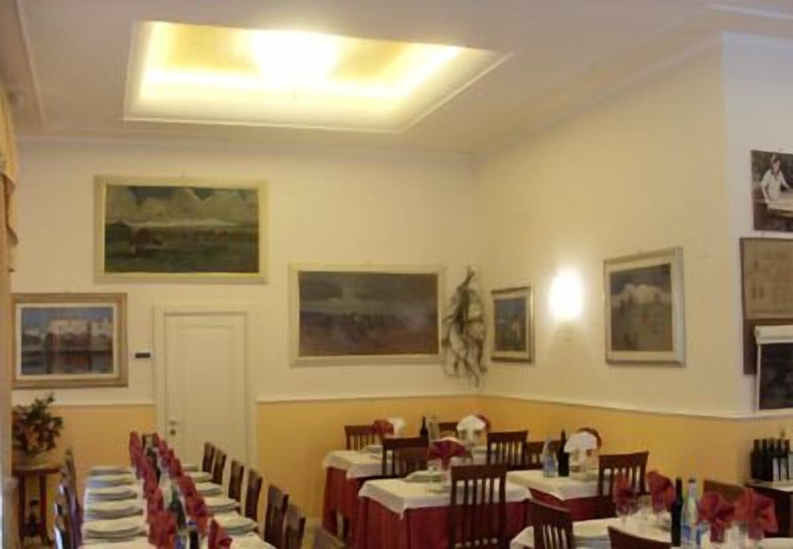 Zona pranzo con tavoli apparecchiati per un pasto, opere d'arte incorniciate alle pareti e un lampadario.