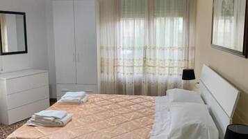 Une chambre d’hôtel avec un lit, une table de chevet, une lampe, une armoire et une fenêtre avec des rideaux.