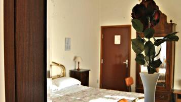 A bedroom with a bed, a nightstand, a lamp, a dresser, and a vase with a rose.