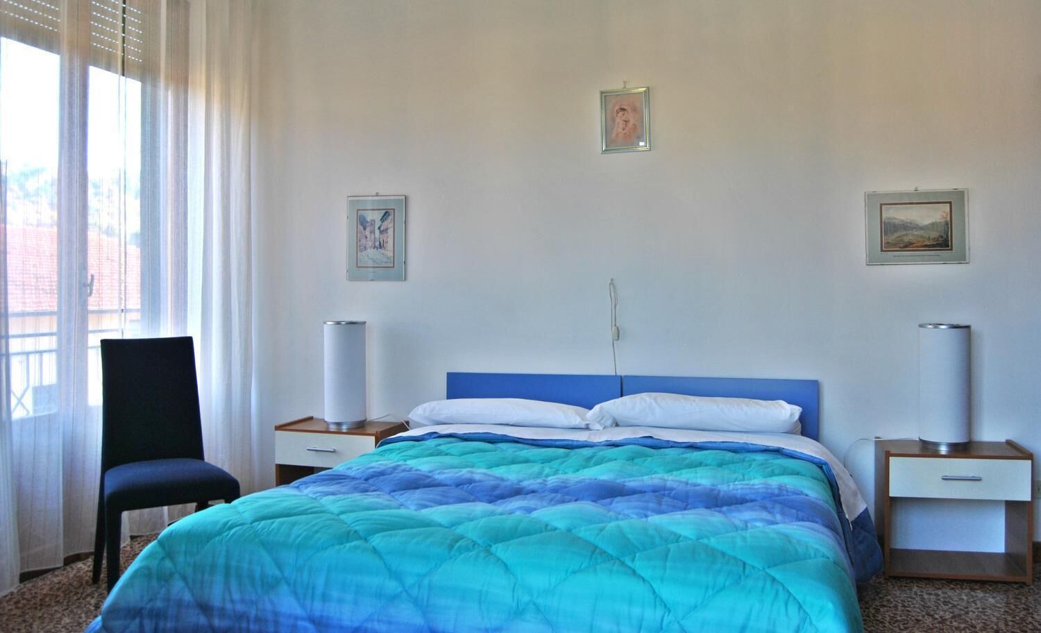 Un dormitorio con una cama, dos mesitas de noche, una silla y dos lámparas de pared.