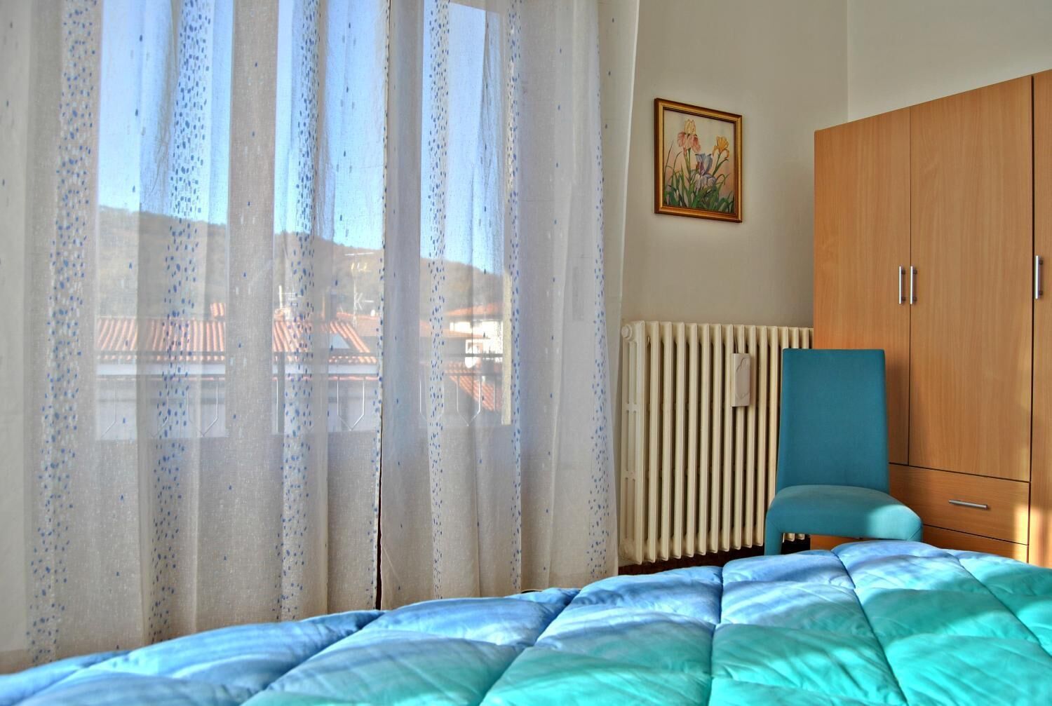 Une chambre à coucher avec un lit, un radiateur, une fenêtre avec des rideaux, une armoire et un tableau accroché au mur.