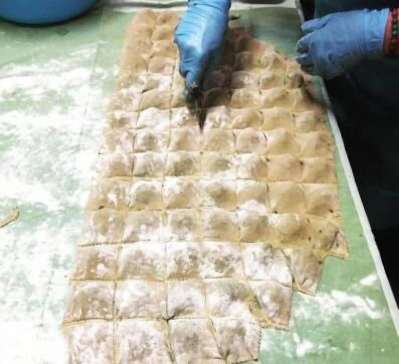 A person handling a large, rectangular, grid-patterned food item on a green surface.