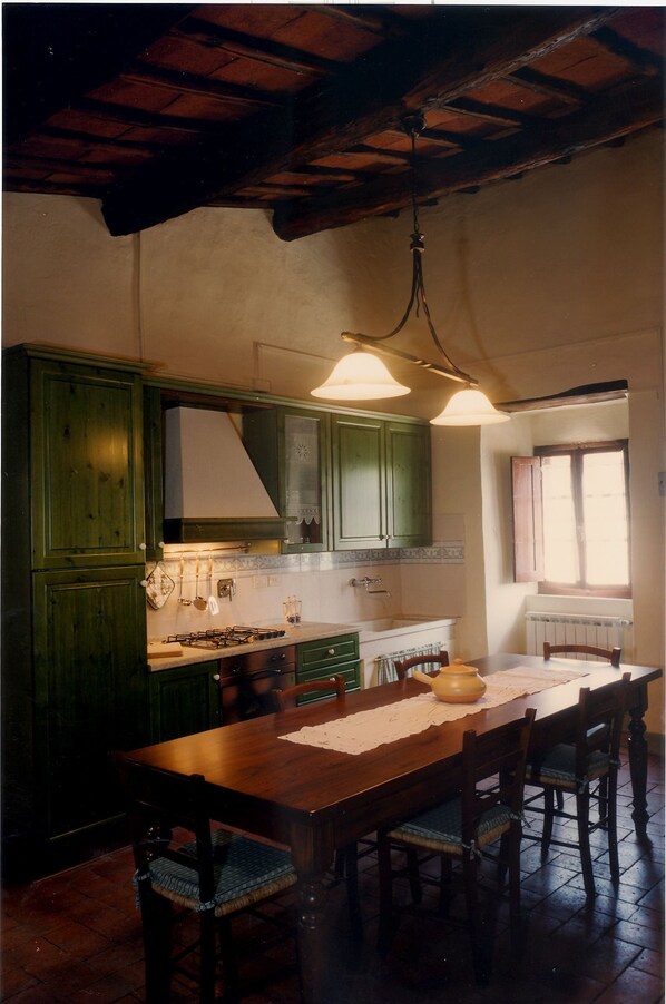 A rustic kitchen with wooden cabinets, a gas stove, and a dining table with chairs. - Borgo Montefolchi (San Casciano in Val di Pesa)