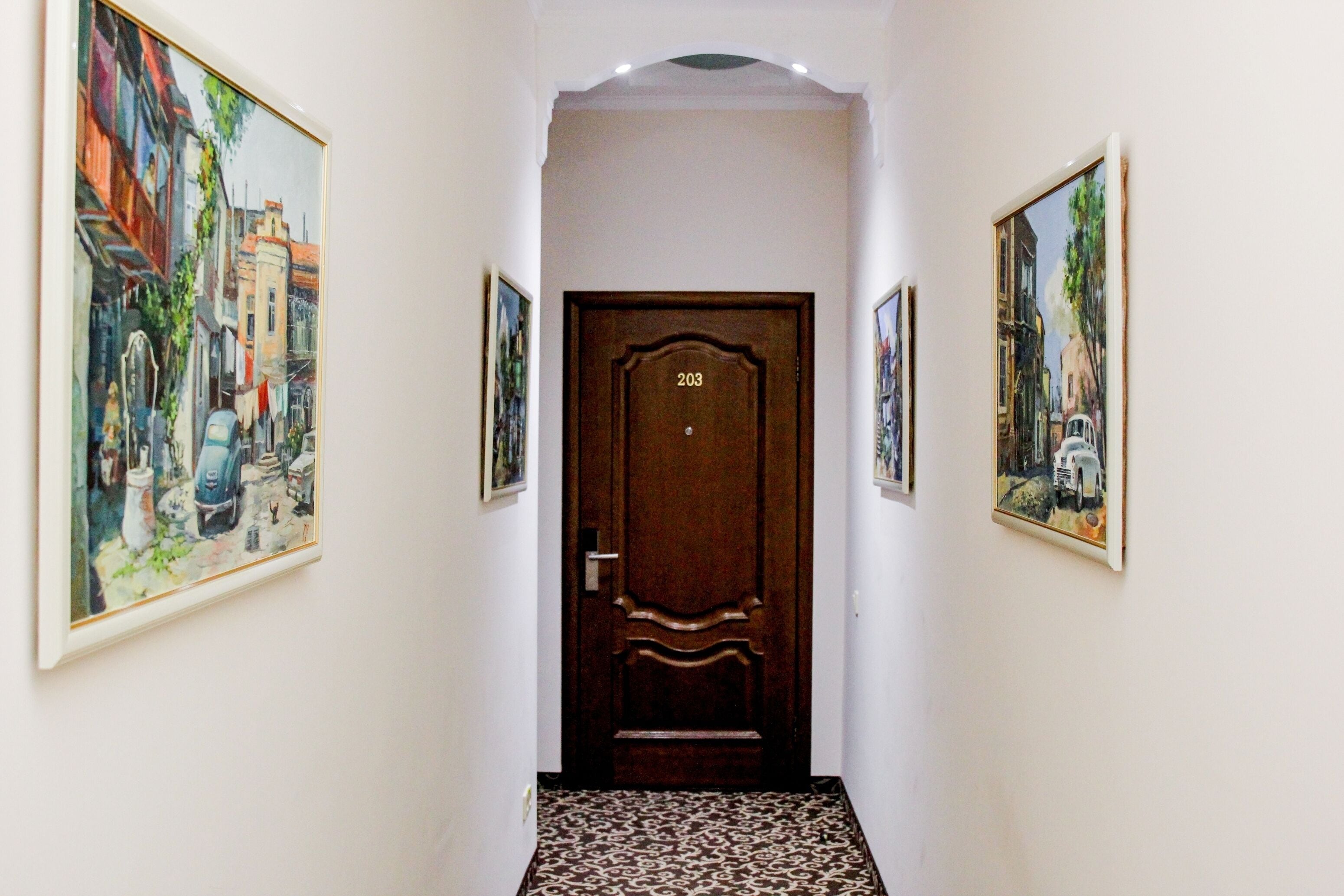 A hallway with a wooden door marked 203, flanked by two framed paintings.