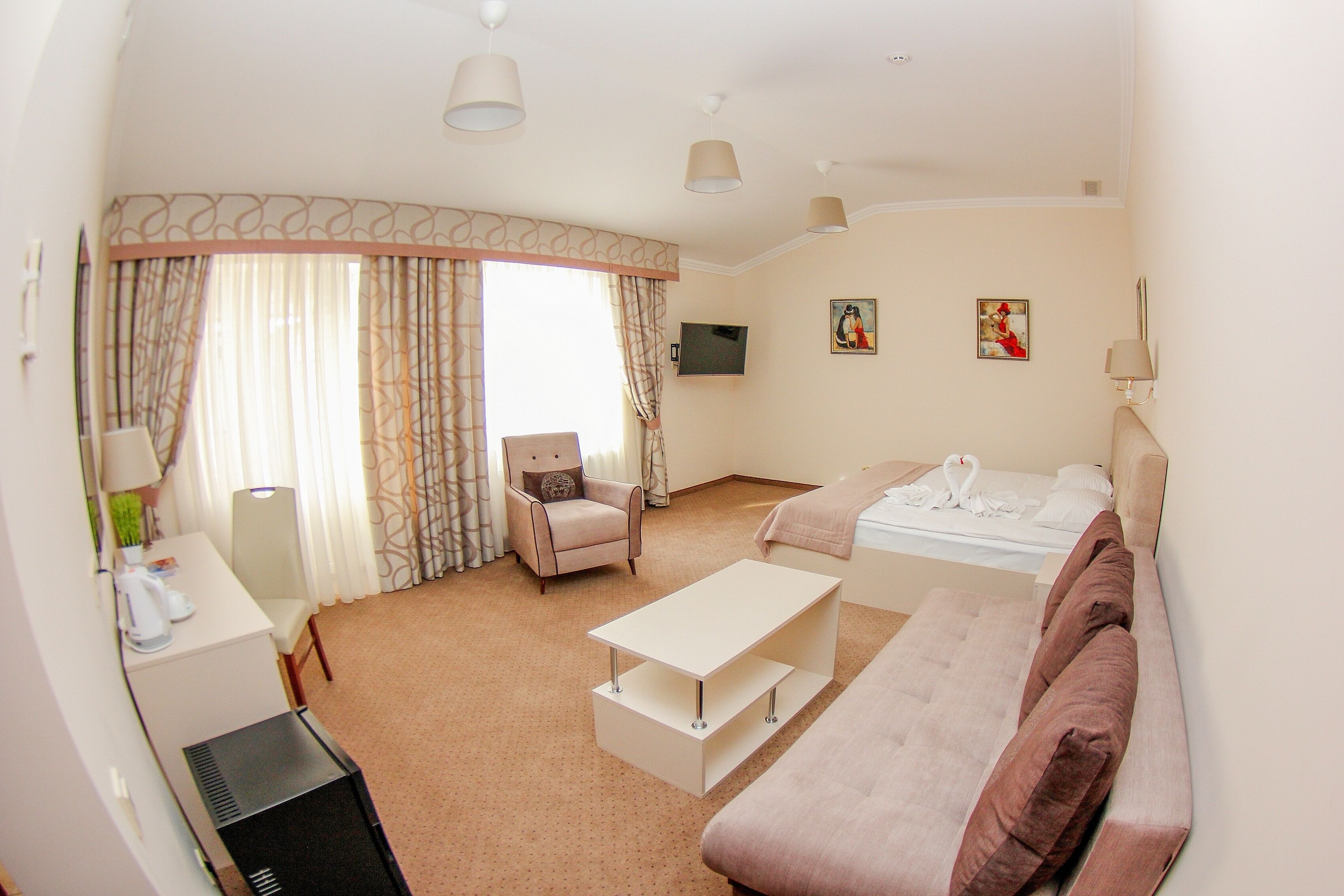 A hotel room with a bed, a sofa, a desk, a chair, and a TV.