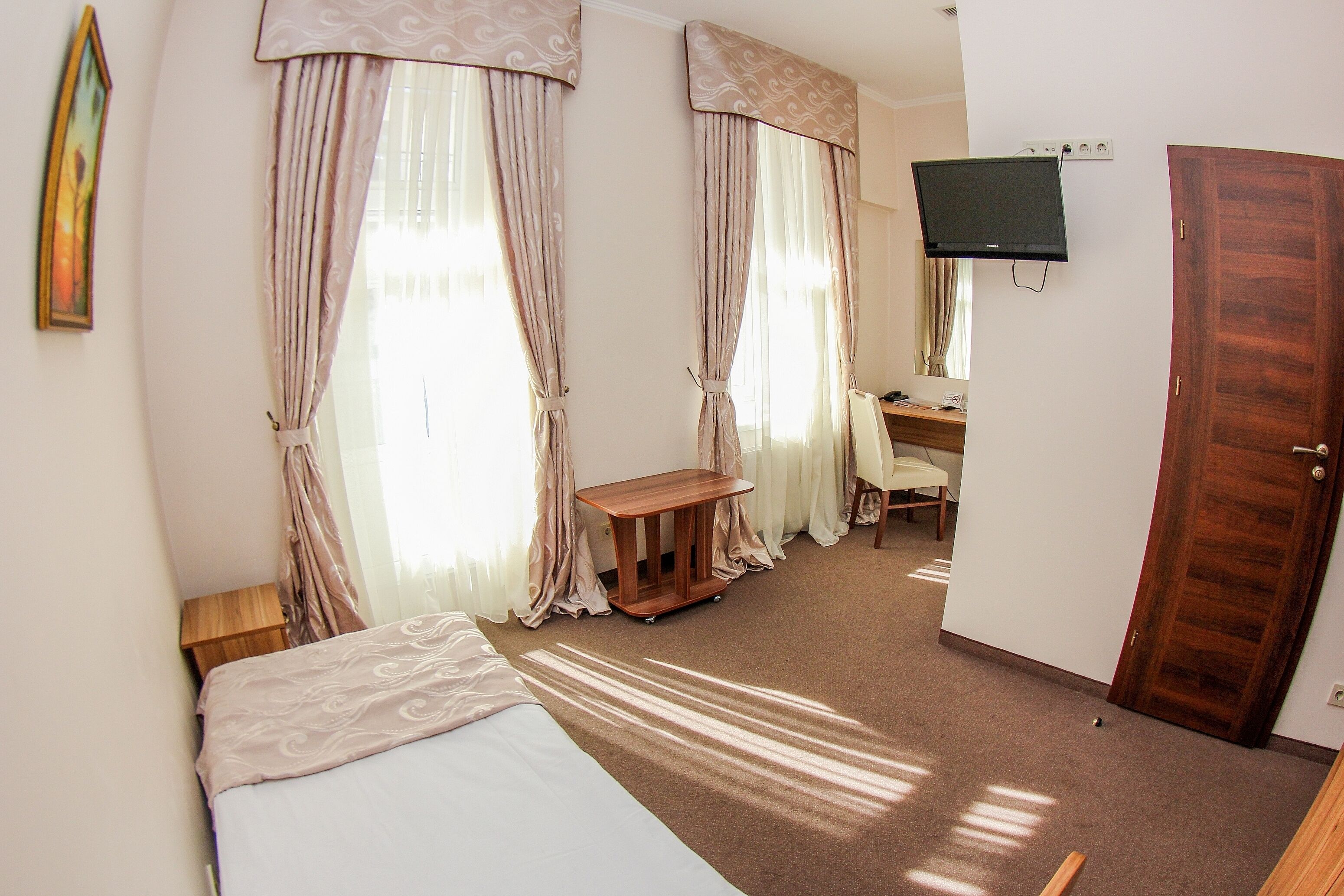 A hotel room with a bed, a desk, a chair, a television, and curtains.