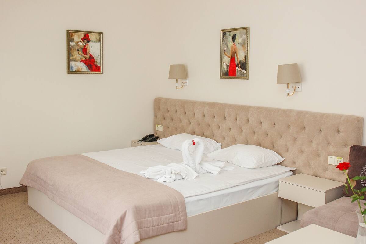 A hotel room with a large bed, two wall-mounted lamps, and two paintings on the wall.