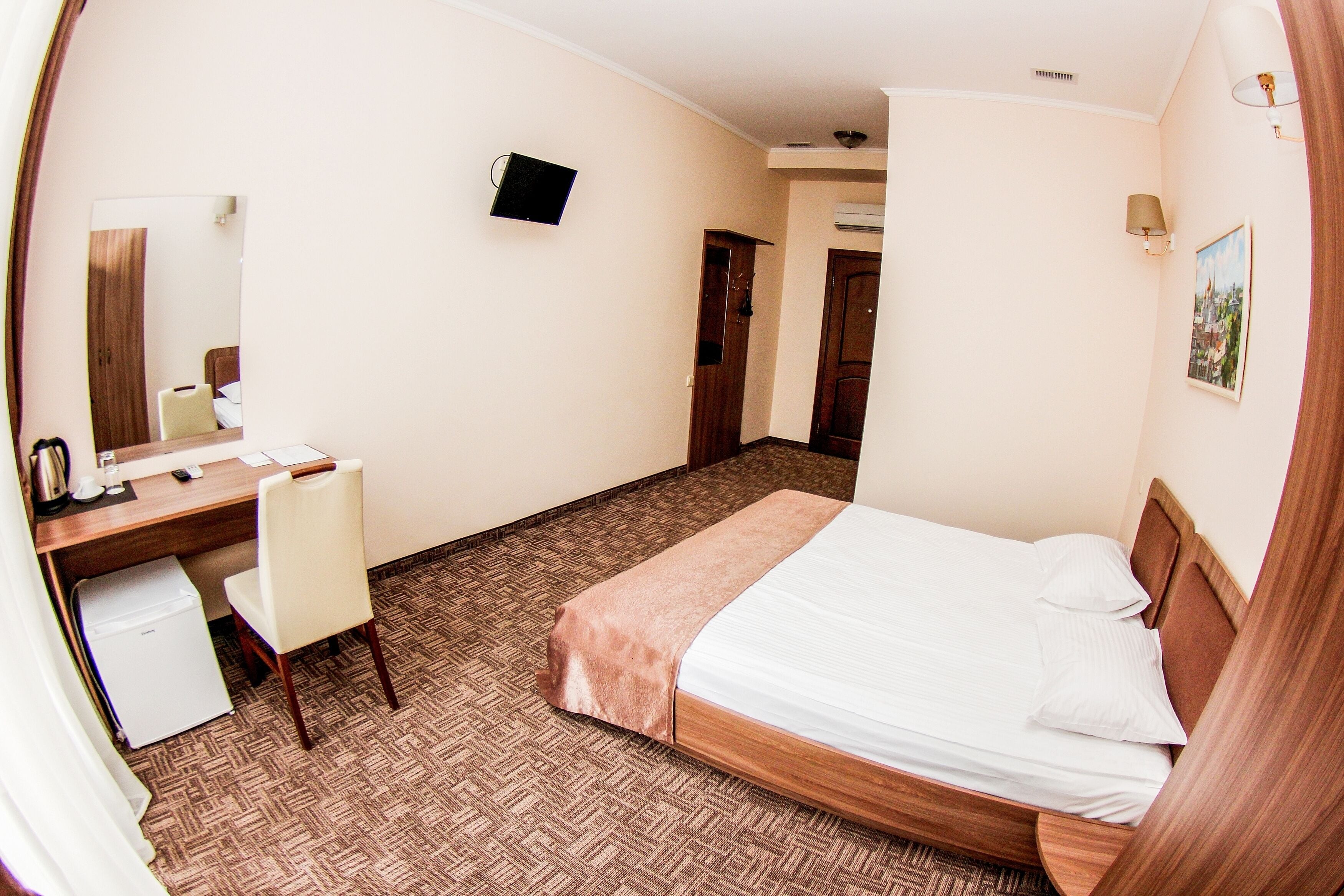 Habitación de hotel con cama, escritorio, silla, refrigerador pequeño, televisor y un cuadro en la pared.