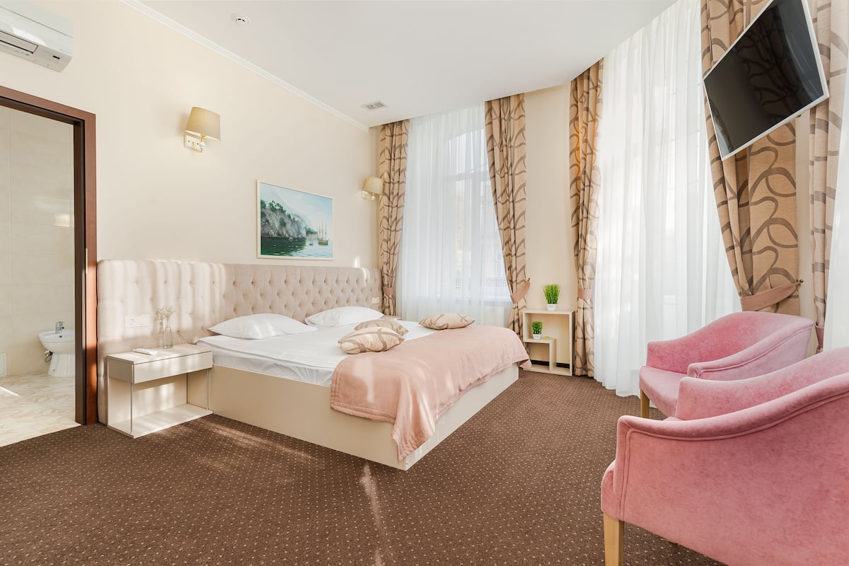 A hotel room with a bed, bedside tables, a TV, a chair, and a window with curtains.