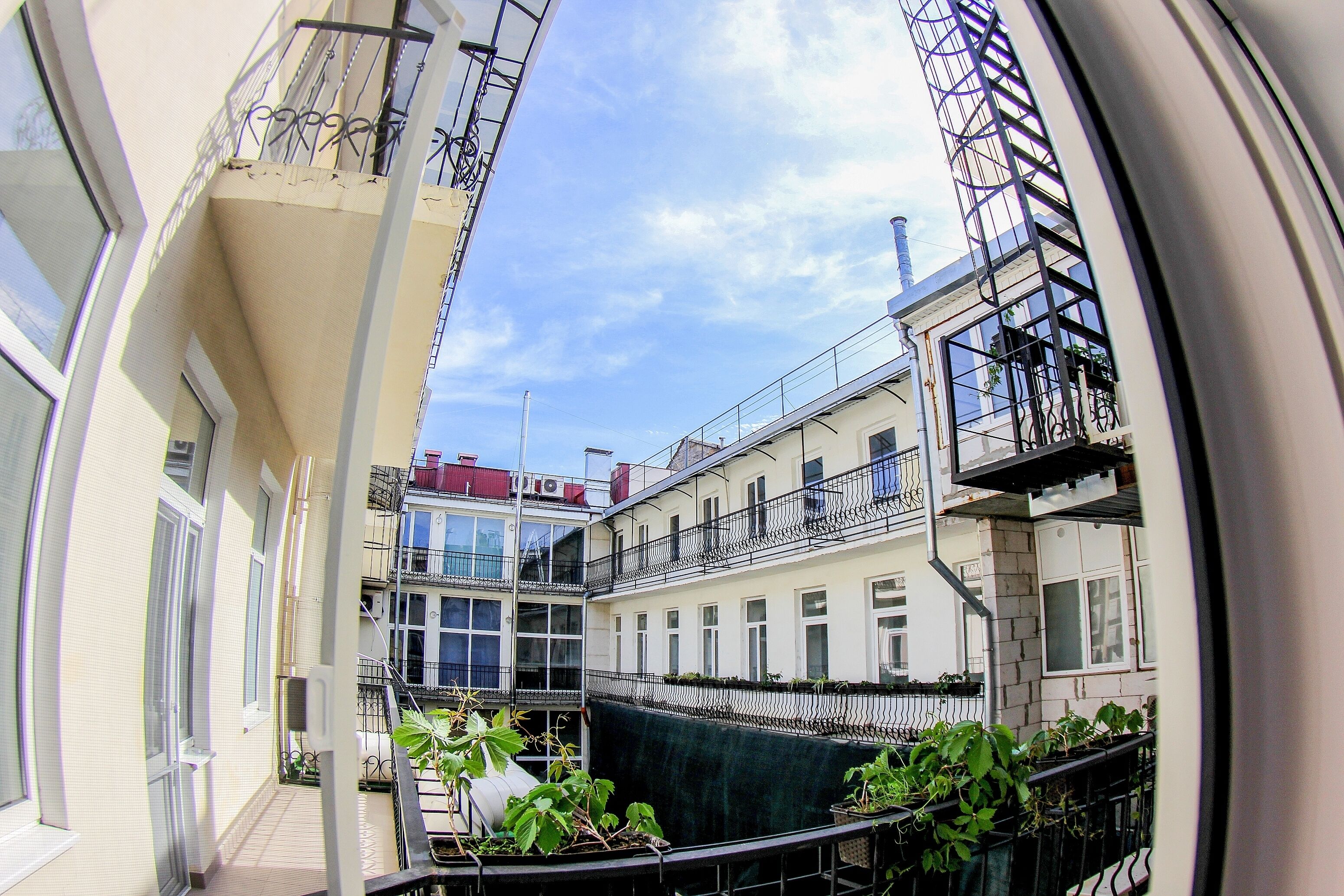 A narrow urban courtyard with balconies, a central green area, and buildings with multiple stories and windows.