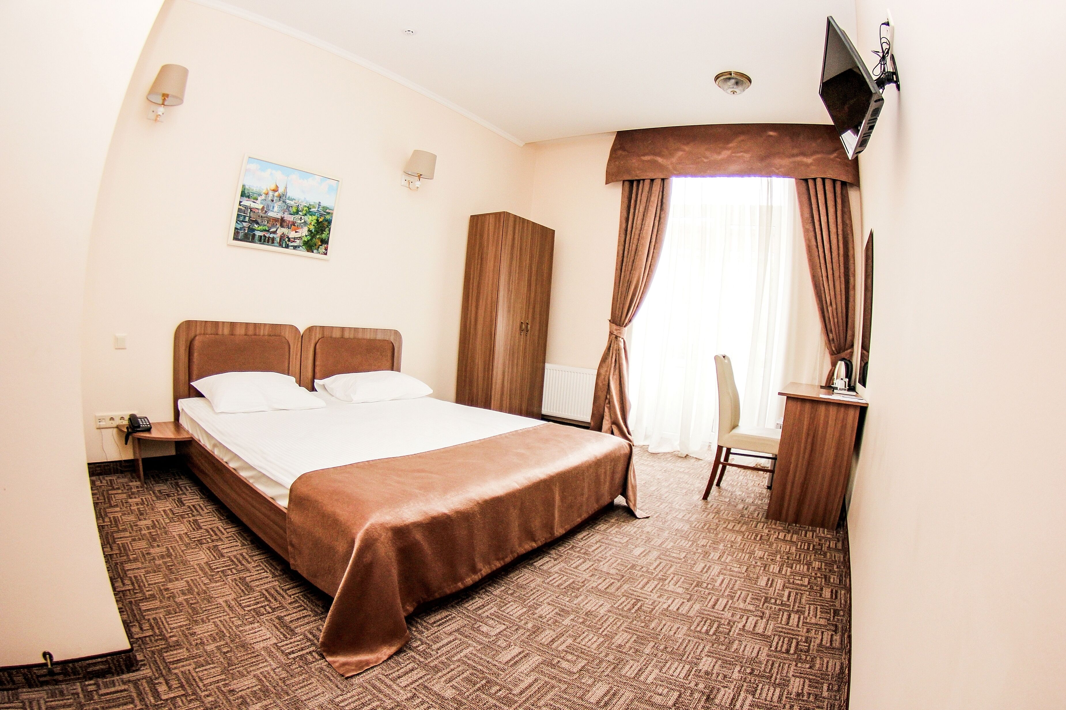 Una habitación de hotel con una cama grande, un escritorio, una silla, un televisor y un cuadro en la pared.