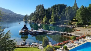 A lakeside marina with boats docked, a swimming pool, and a forested hillside in the background. - Bahia Manzano Resort (Villa La Angostura)