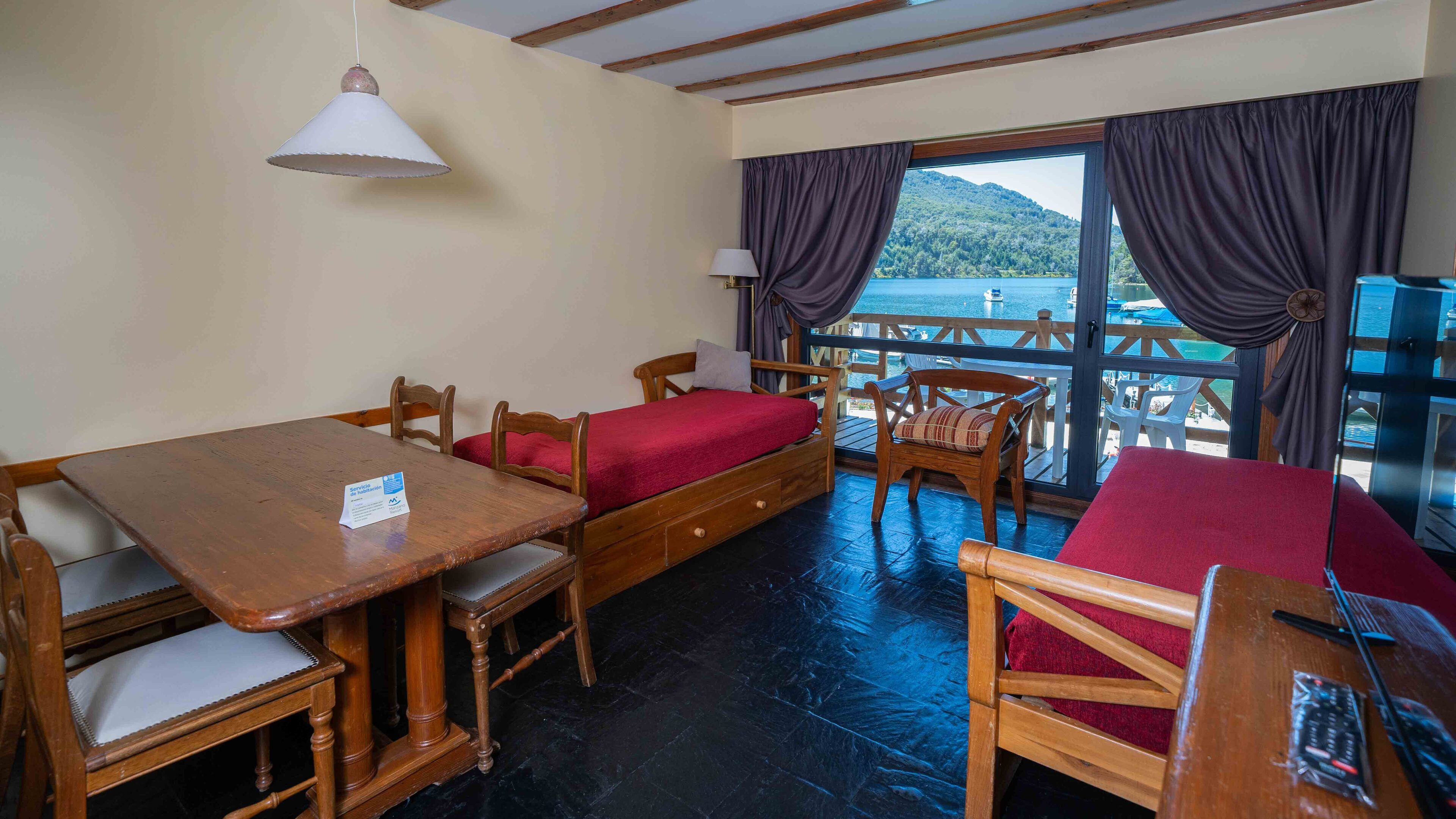 A room with a wooden table, two single beds, a chair, and a view of the sea.