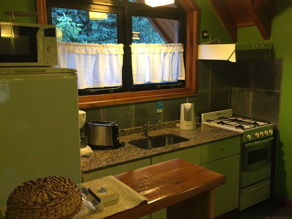 Cocina compacta equipada con microondas, tostadora, pileta, estufa y ventana con cortinas.