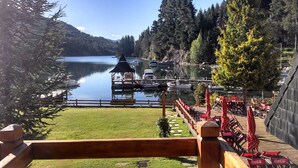 A lakeside view with a wooden deck, outdoor seating, and boats docked at the pier. - Bahia Manzano Resort (Villa La Angostura)