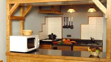 A kitchen with a microwave, a pot on the stove, and a bowl of fruit on the counter.