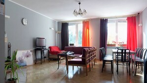 A living room with a sofa, a TV, a dining table with chairs, a chandelier, and a potted plant. - Anton House (Warsaw)