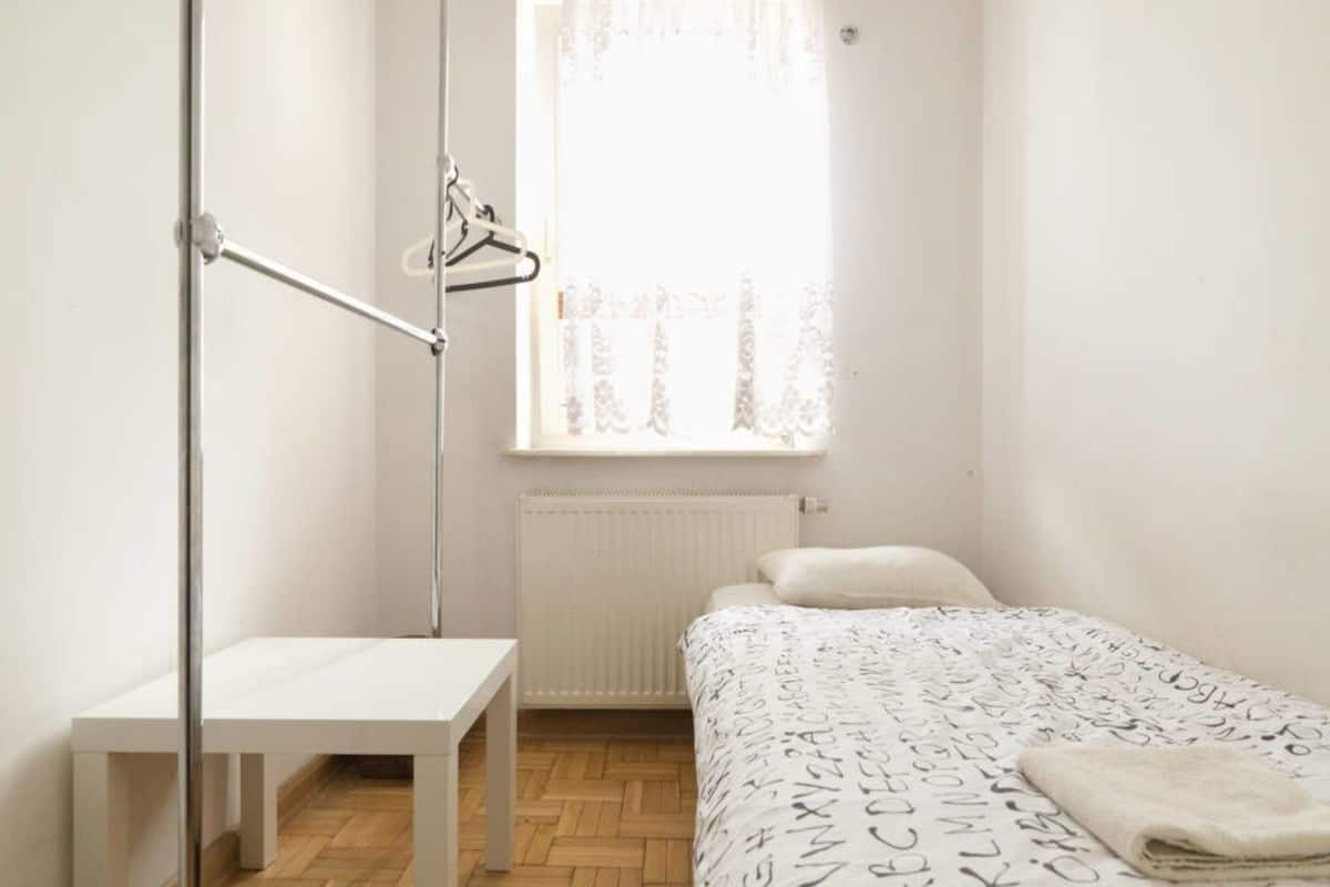 A small, bright room with a bed, a white table, and a radiator.