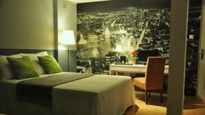 A hotel room with a bed, a desk, and a chair. There is a cityscape mural on the wall behind the bed. - Anton House (Warsaw)