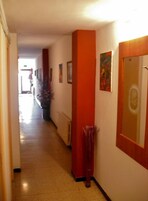 Un pasillo con suelo de baldosas, un radiador y una puerta con espejo.