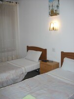 Habitación de hotel con dos camas individuales, una mesita de noche, una lámpara y un cuadro en la pared.