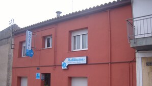 Un edificio de fachada roja, con un letrero que dice 'Habitaciones' e indicando las habitaciones, y un letrero de 'Hostal' sobre la entrada.